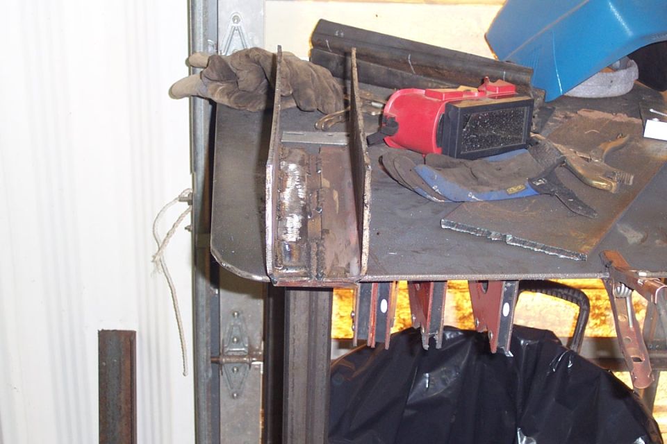 Steel fabricated brackets and work gloves on a garage workbench