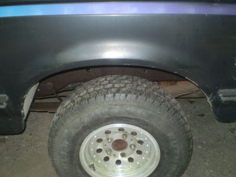 1979 Ford Bronco - Close-up of the rear wheel well and tire on a dark SUV, a blue accent stripe and aftermarket wheels.