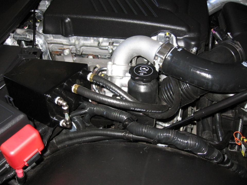 Engine bay close-up of turbocharged four-cylinder with aluminum intake elbow and hoses