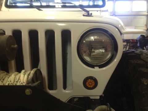 2000 Jeep TJ - Close-up of a white Jeep Wrangler's front grille, highlighting the iconic vertical slots and a round headlight with an amber blinker below.…