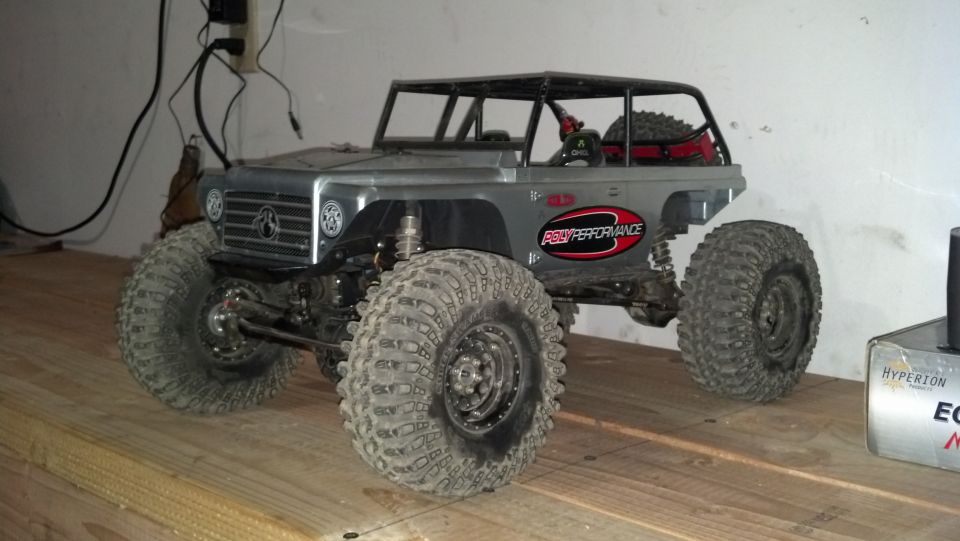 RC rock crawler with big tires and roll cage, sitting on a wooden surface