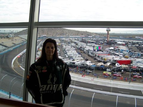 1981 Ford Bronco - A woman stands in front of a large window overlooking a busy speedway, with numerous RVs and vehicles parked in the lot.