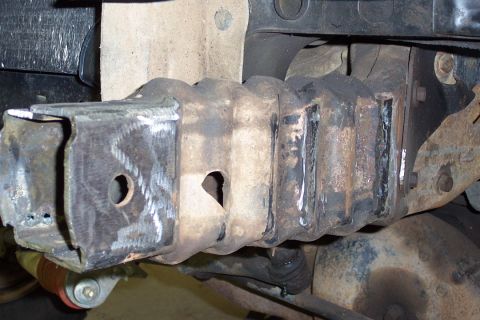 1996 Ford Bronco - Underside view of a vehicle frame section showing a boxed steel frame member with drilled holes and multiple weld beads. Fresh weld seams a…