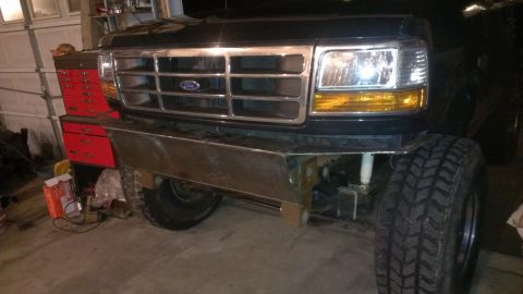 1995 Ford Bronco - Front view of a black Ford truck with a custom bumper and off-road tires, parked indoors.
