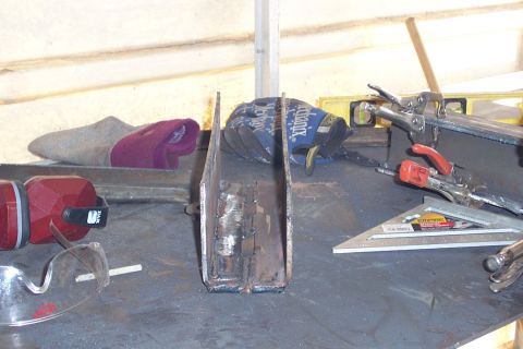 1996 Ford Bronco - A welded steel channel-metal bracket or fabricated part sits on a dark metal workbench, surrounded by tools including locking pliers/clamps…