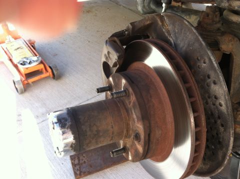 1989 Ford Bronco - Close-up of a vehicle's brake assembly, showing a rusty rotor and caliper, with a hydraulic jack visible.