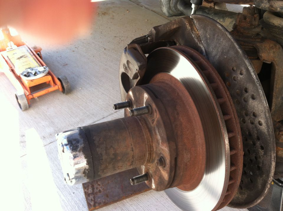Rusty vehicle brake rotor and caliper assembly with a hydraulic jack in the background