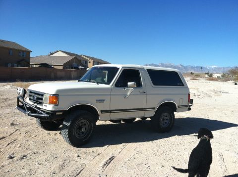 1989 Ford Bronco - A white Ford Bronco sits parked in a dusty, arid landscape under a clear blue sky.