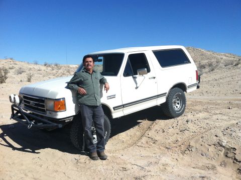 1989 Ford Bronco - A man poses with a white 1989 Ford Bronco equipped with an aftermarket bumper in a desert setting.