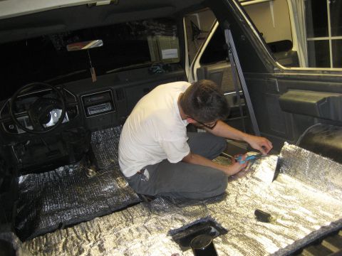 1989 Ford Bronco - A person works on the interior of a vehicle, applying insulation to the floor.