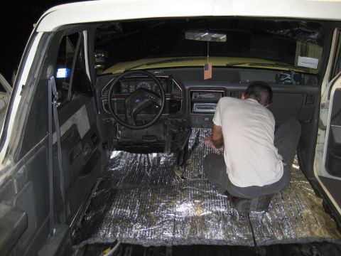 1989 Ford Bronco - A person is installing insulation on the floor of a vehicle's interior, likely for sound dampening.