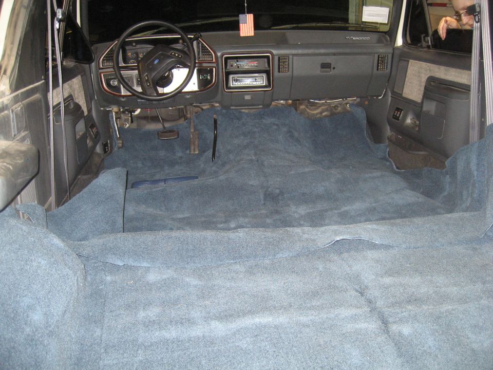 Interior of a 1989 Ford Bronco with blue carpet installed. Shows dashboard, steering wheel, and front seats