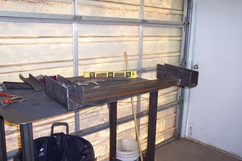 1996 Ford Bronco - A homemade steel workbench sits against a metal garage-door wall, holding a yellow spirit level, a wooden-handled tool, and a metal tray; r…