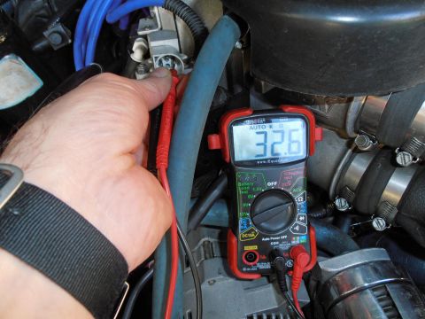 1990 Ford Bronco - A multimeter displays a reading of 32.6 ohms while being used to test a component in an engine bay.