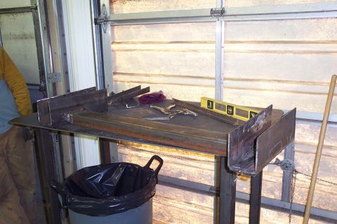 1996 Ford Bronco - A metal welding or fabrication workbench in a garage holds a yellow spirit level, locking pliers, and a purple rag, with a black-lined tras…