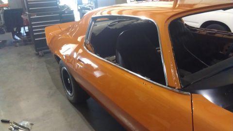 1973 Chevrolet Camaro - The interior of an orange 1973 Chevrolet Camaro is visible from the driver's side, showing the black seats and door frame.
