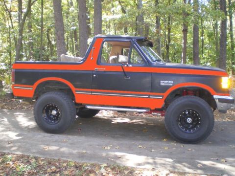 1994 Ford Bronco - This lifted Ford Bronco features a two-tone paint scheme with orange accents and black wheels.