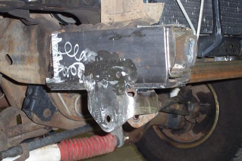 1996 Ford Bronco - Close-up underside view of a fabricated steel bracket or mount welded to a frame crossmember, showing fresh weld beads and bare metal with…