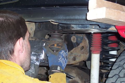 1996 Ford Bronco - Underside view of a vehicle's front suspension being worked on, showing a coil spring, a white-bodied shock absorber with a red boot, and r…