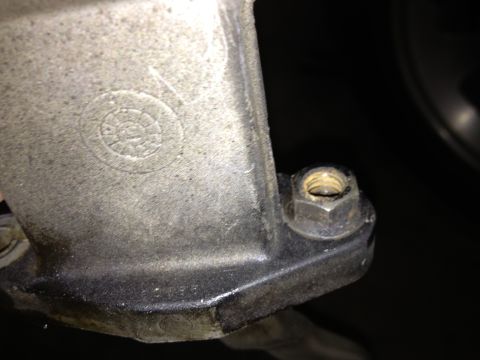 1978 Ford Bronco - A close-up view of a metal component, showing a bolt and nut attachment and an embossed circular marking.