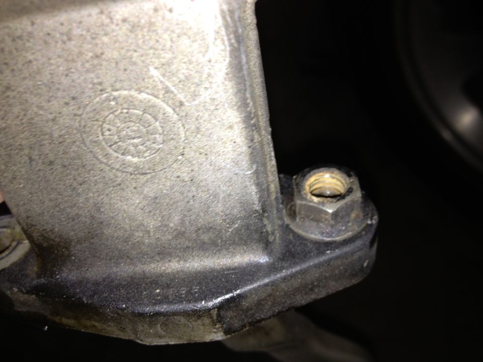 Close-up of a metal casting with a bolt and nut. There's a circular embossed mark on the casting