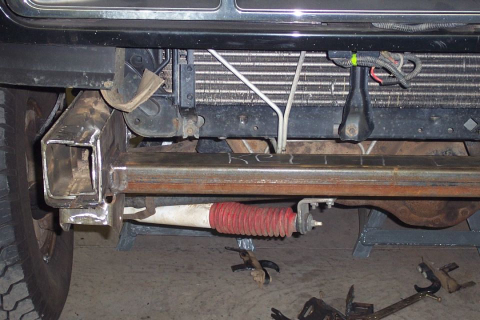 Underside front axle of a Bronco with red-booted damper on jack stands