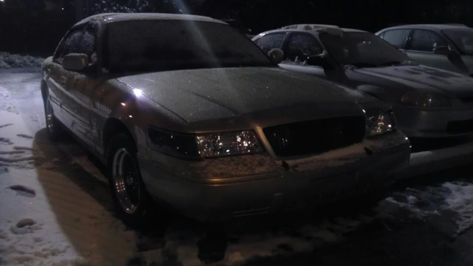 Silver 2000 Mercury Grand Marquis covered in snow, parked in a lot at night