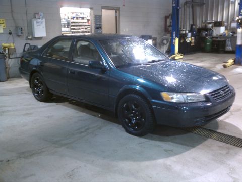 1998 Toyota Camry - A dark teal sedan with black wheels is parked inside a garage, with water droplets visible on its exterior.