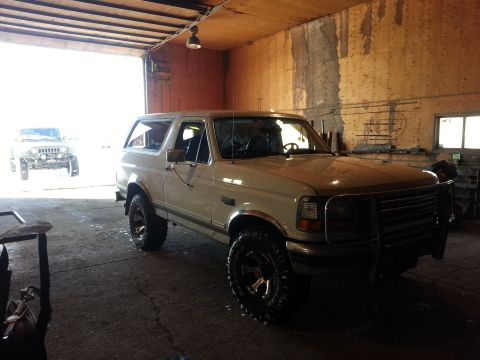 1994 Ford Bronco - A white 1994 Ford Bronco is parked inside a garage, with another vehicle visible in the background.