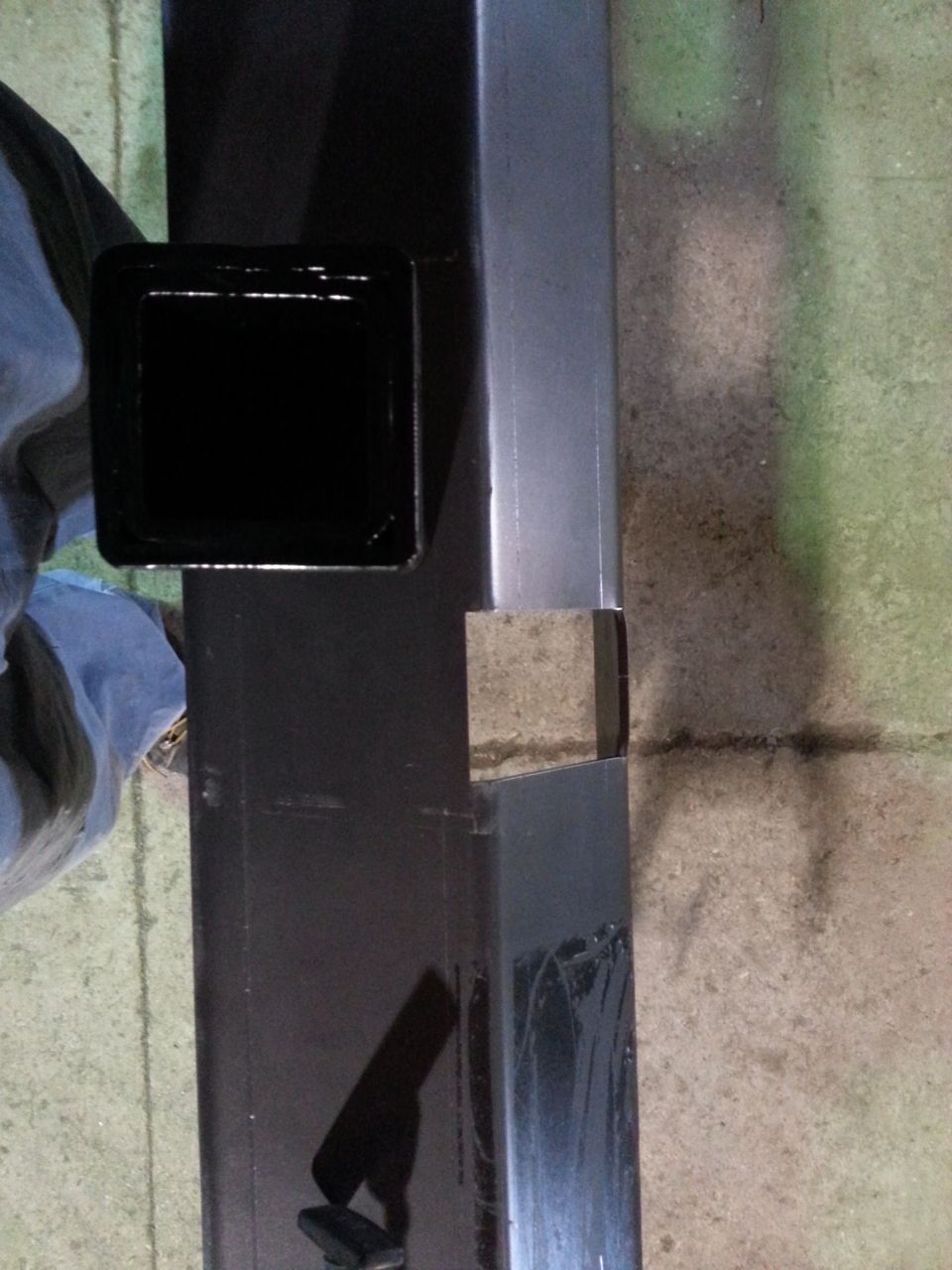Black trailer hitch receiver with a square opening, attached to a metal frame. A blue cloth is visible to the left