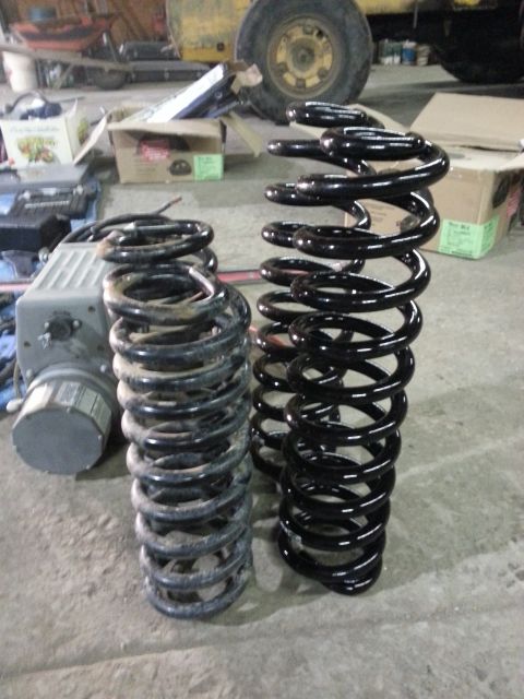 1994 Ford Bronco - A pair of coil springs, one showing wear and the other appearing new, are displayed on a workshop floor.