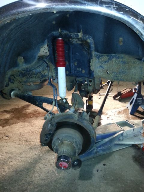 1994 Ford Bronco - Close-up of a vehicle's front suspension and wheel hub assembly, a red-topped shock absorber.