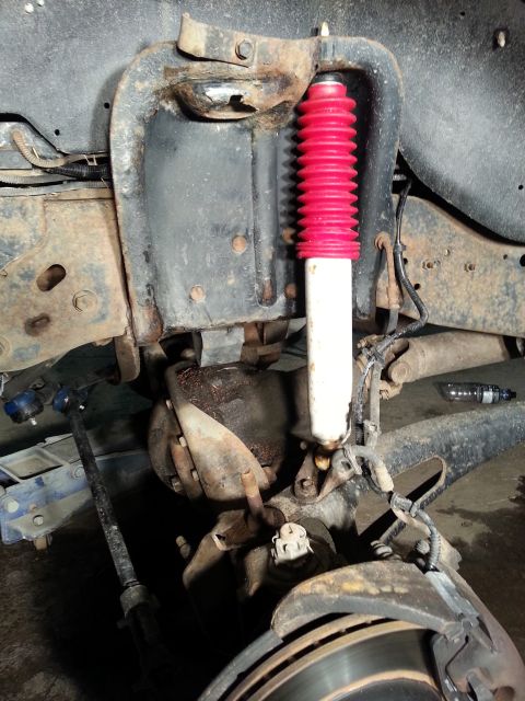 1994 Ford Bronco - The front suspension system of a vehicle is shown, a red and white shock absorber and brake components.