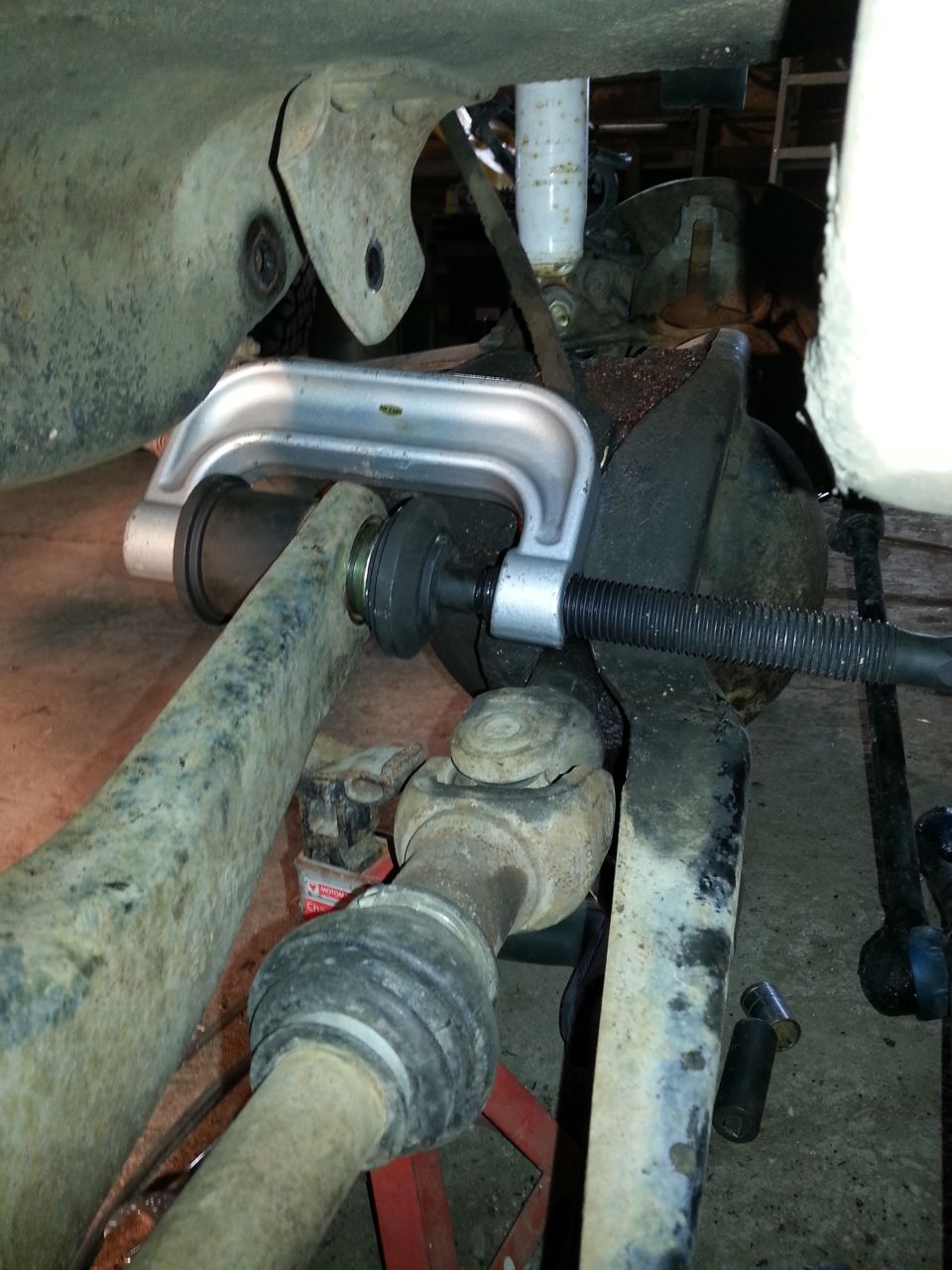 Ball joint press tool compressing a suspension component, with driveshaft visible