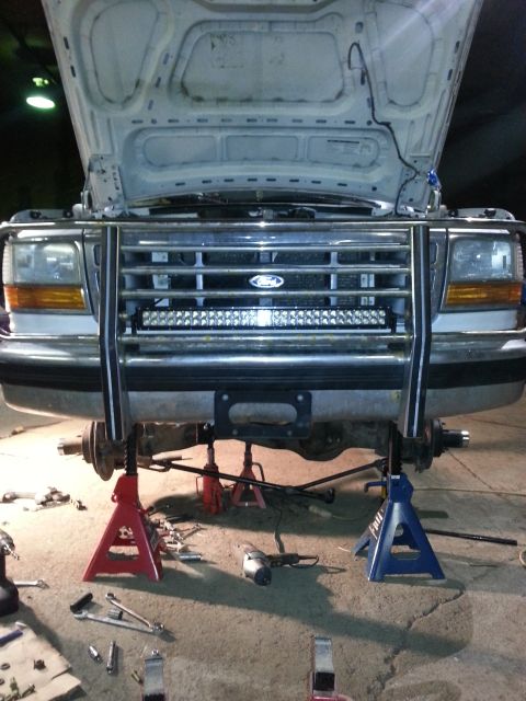 1994 Ford Bronco - Front view of a 1994 Ford Bronco with its hood open and front end raised on jack stands for maintenance.