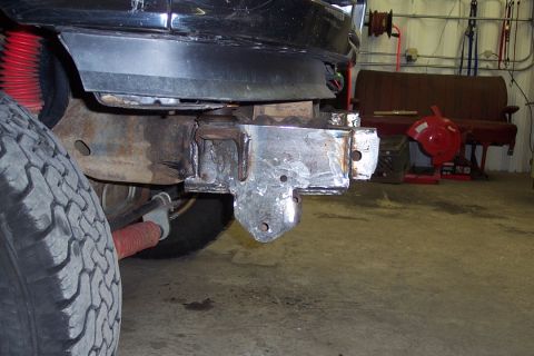 1996 Ford Bronco - Low-angle underside view of a dark-colored Ford Bronco showing a freshly fabricated/welded steel front frame bracket or mounting plate, wit…