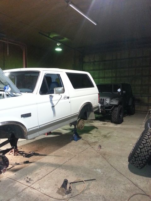 1994 Ford Bronco - Two SUVs, a white Ford Bronco and a black Jeep Wrangler, are parked inside a garage.