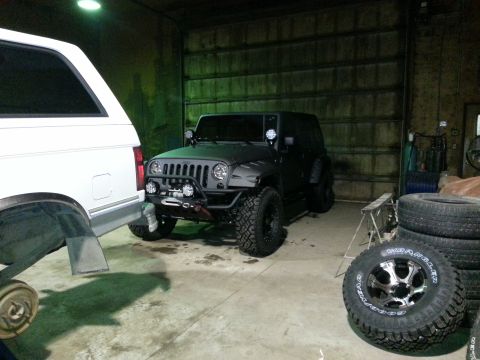 1994 Ford Bronco - A dark-colored Jeep Wrangler is parked inside a garage next to a white SUV, with spare tires visible.