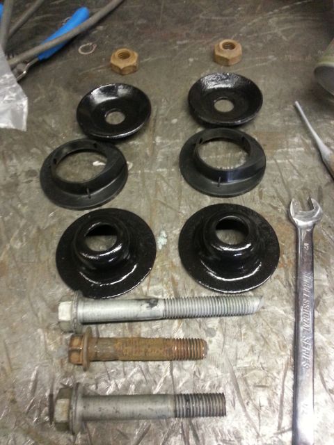 1994 Ford Bronco - A collection of suspension components and bolts are laid out on a workbench, with a wrench nearby.