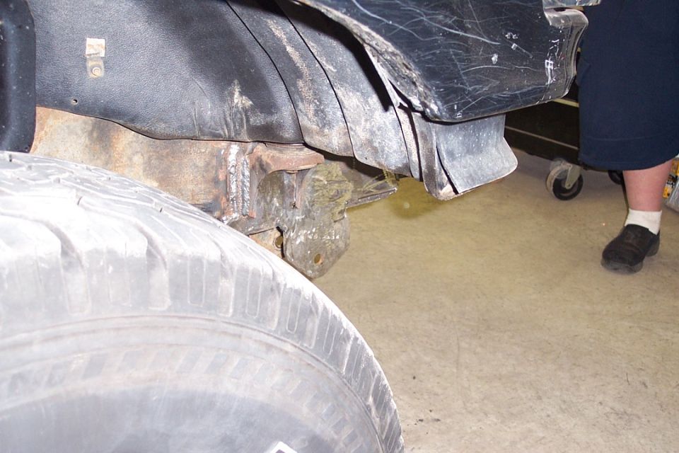 Rusty vehicle frame rail and fender liner with spare tire in a shop