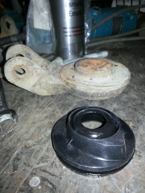 1994 Ford Bronco - A rusty metal suspension part and a new black rubber component sit on a wooden surface.