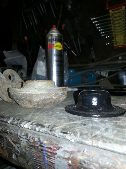 1994 Ford Bronco - A new black rubber car part sits beside an old, worn metal car part on a cluttered workbench.