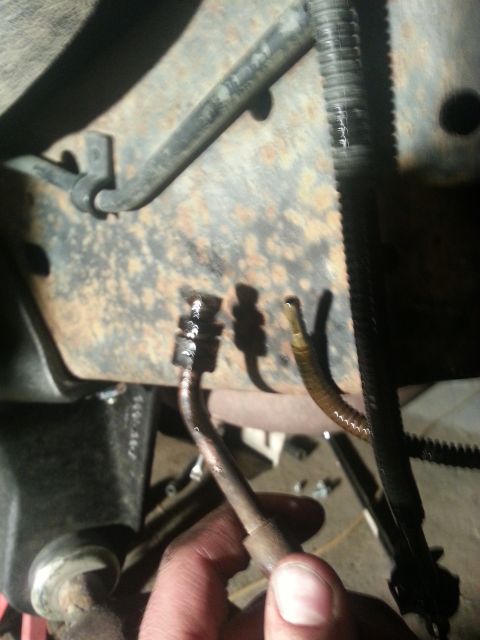 1994 Ford Bronco - A hand disconnects a brake line from a heavily rusted vehicle frame.