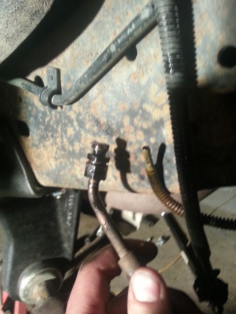 1994 Ford Bronco - A hand disconnects a brake line from a vehicle's undercarriage.