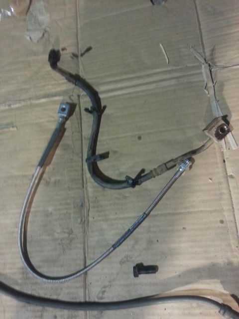 1994 Ford Bronco - Two brake hoses and a bolt are laid out on a cardboard surface.