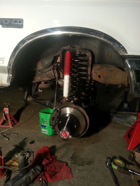 1994 Ford Bronco - Front suspension of a white Ford Bronco undergoing repair, with tools and equipment scattered around.