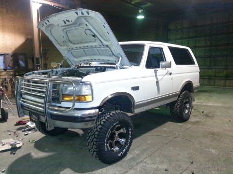 1994 Ford Bronco - White Ford Bronco parked indoors with its hood up, showing off its lifted suspension and front end.