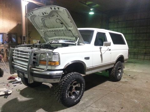 1994 Ford Bronco - This lifted Ford Bronco is parked inside a garage with its hood open, revealing the engine bay.
