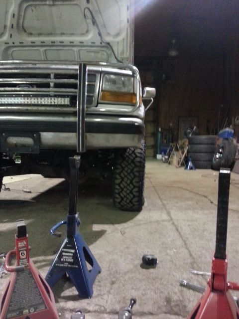 1994 Ford Bronco - A Ford truck is raised on jack stands in a garage, showing its front end and large off-road tires.