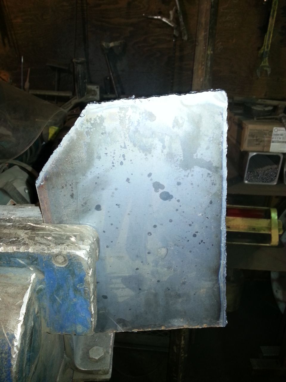 metal piece clamped in blue vise, workshop background